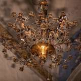 Dal centro del soffitto cade poi un raffinato candelabro settecentesco adornato da applicazioni in bronzo dorato a motivo floreale